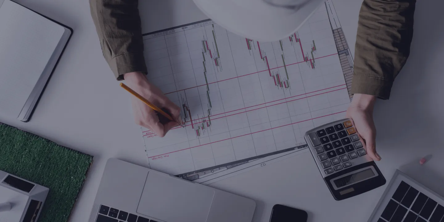 Person reviewing candlestick chart with calculator and pencil at desk