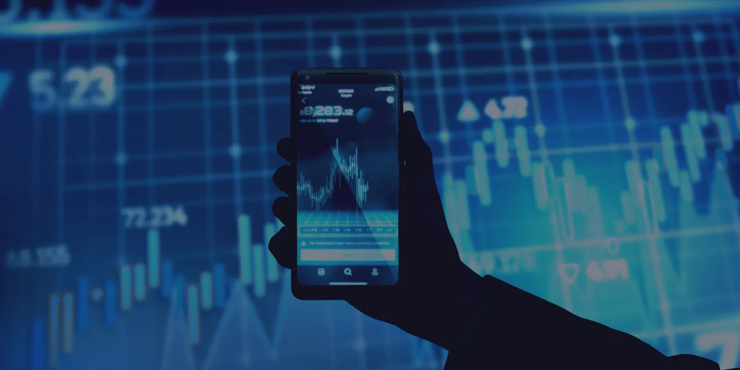 Hand holding smartphone displaying trading chart with price data and candlestick graph