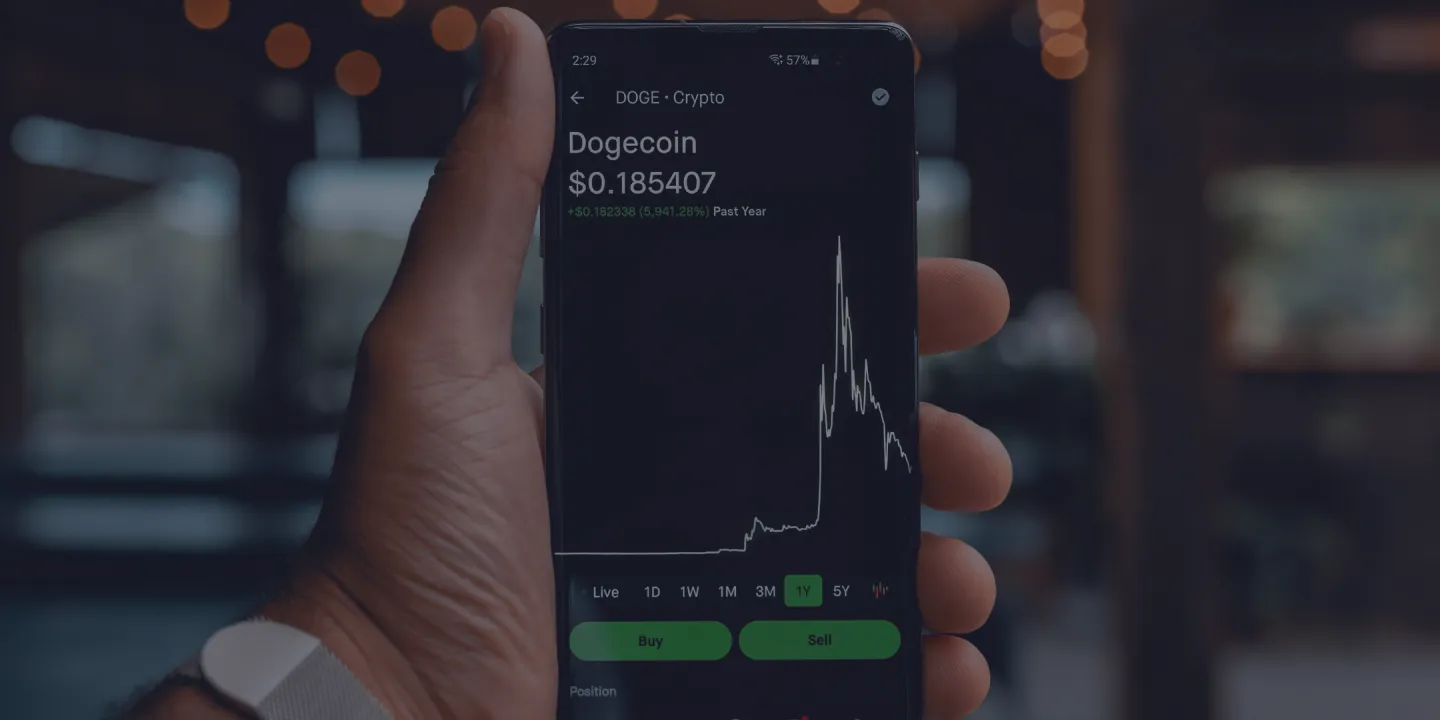 Hand holding smartphone displaying Dogecoin price chart and trading interface
