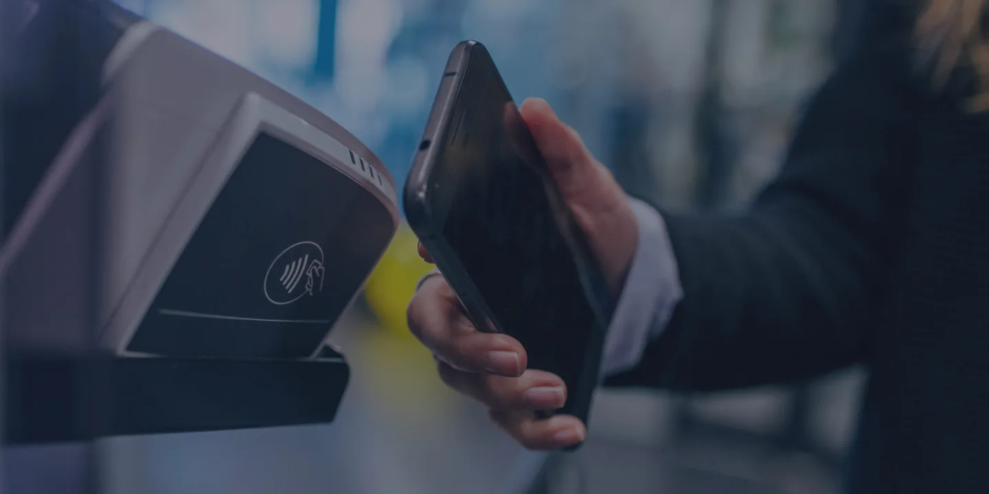 Hand holding mobile payment device near contactless terminal with wireless icon