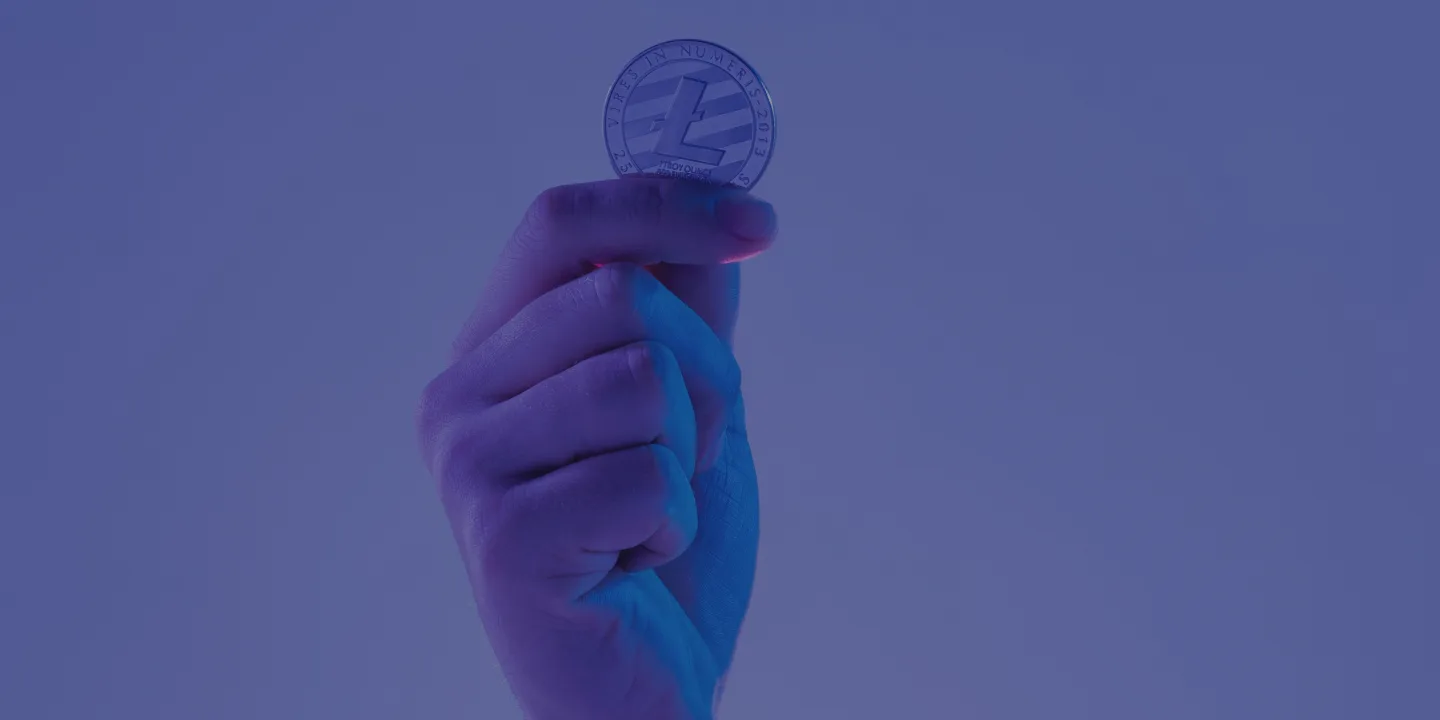 Hand holding Litecoin cryptocurrency token against purple blue gradient background