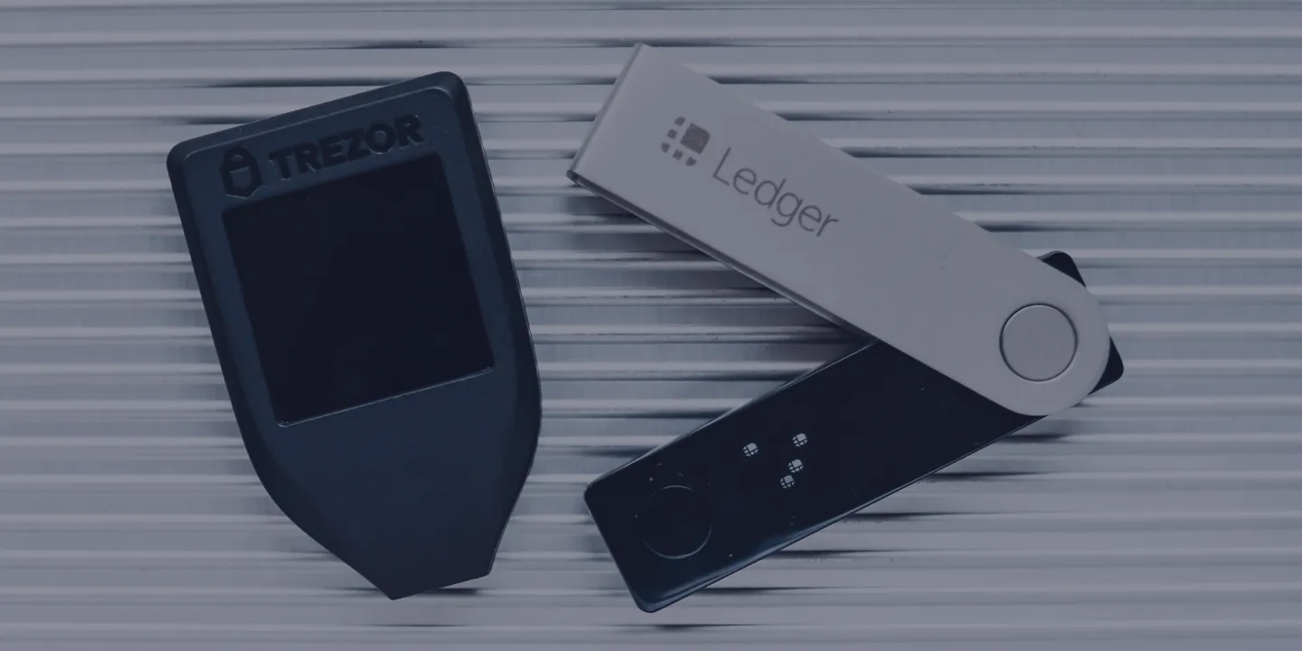 Trezor and Ledger hardware cryptocurrency wallets on wooden surface