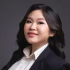 Professional headshot of woman in dark blazer and white shirt against gray background